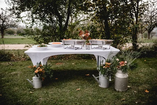 Festlich gedeckter Catering-Tisch im Freien mit Chafing-Dishes und herbstlicher Blumendeko.